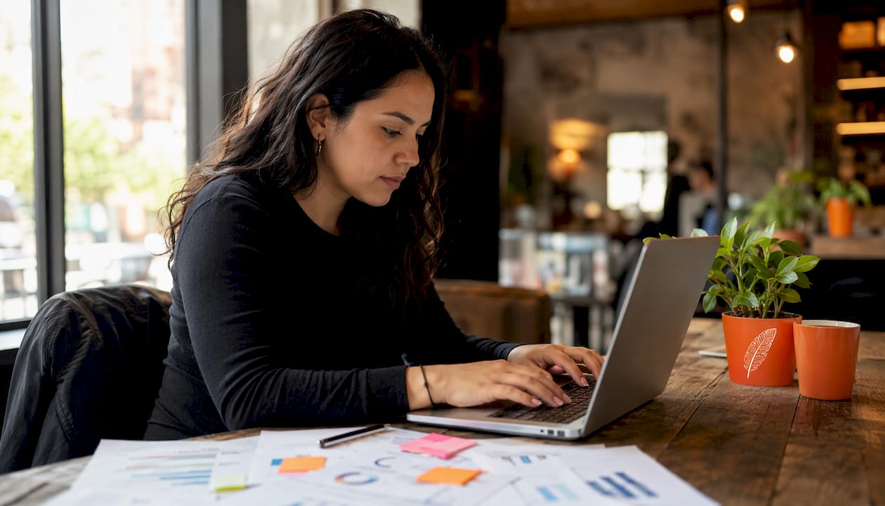 Data scientist typing on laptop with printed charts