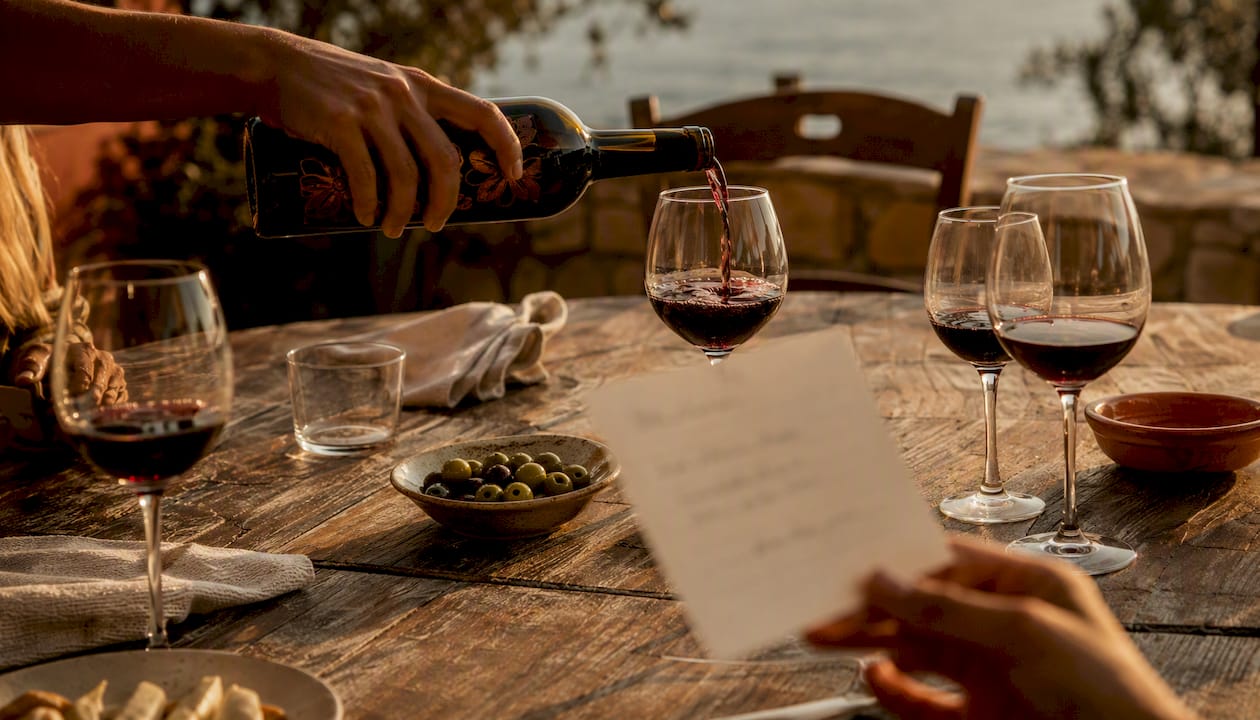 Hands pouring wine with tasting cards on rustic table