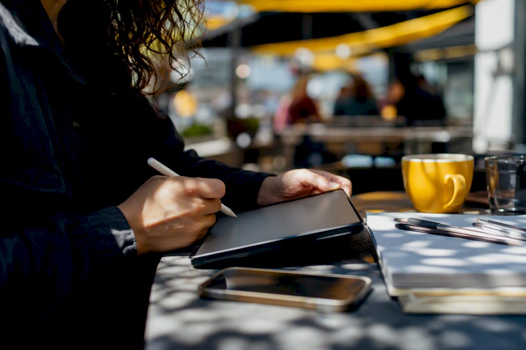 Hands taking notes on tablet with recorder nearby