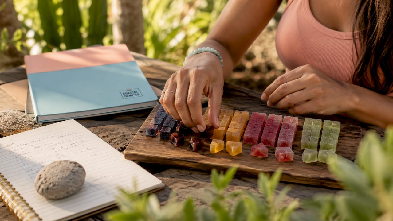 Hands arranging hemp gummies and dose journal