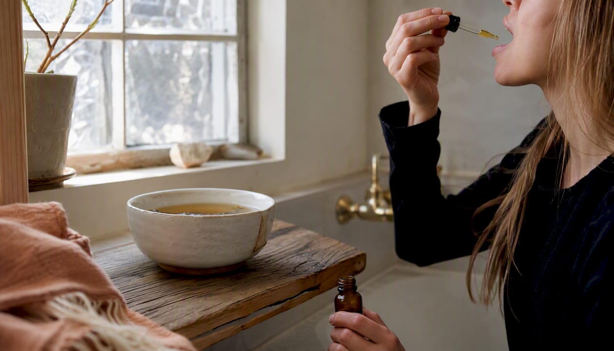 Hand administering hemp tincture near tea in natural bedroom