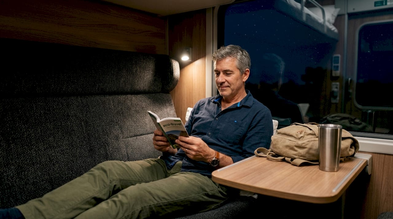Man reading eco-travel guide on night train