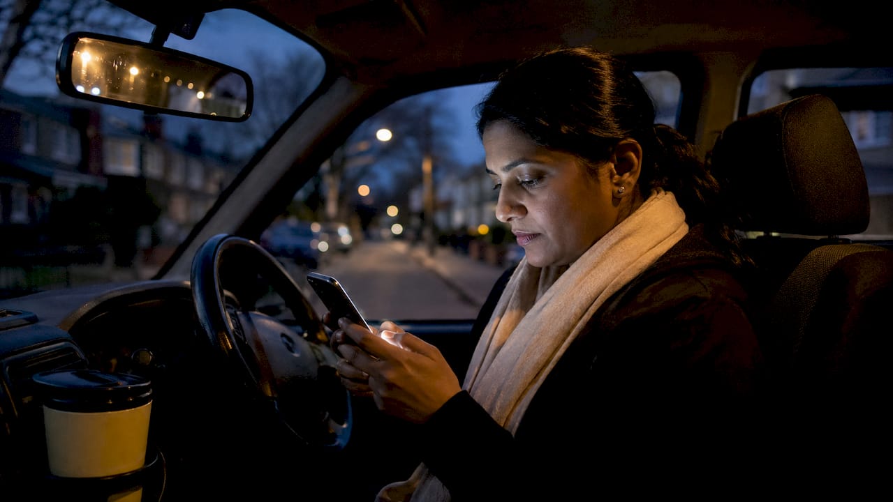 Driver checking TfL emails on smartphone in cab