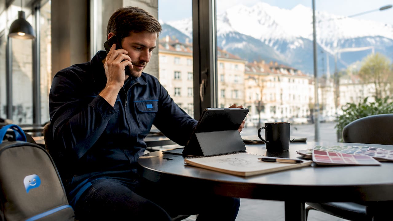 In der Werkstatt nutzt der Mechaniker sowohl sein Smartphone mit Sprachassistent als auch das Tablet, um seine Arbeit im Büro effizient zu organisieren.