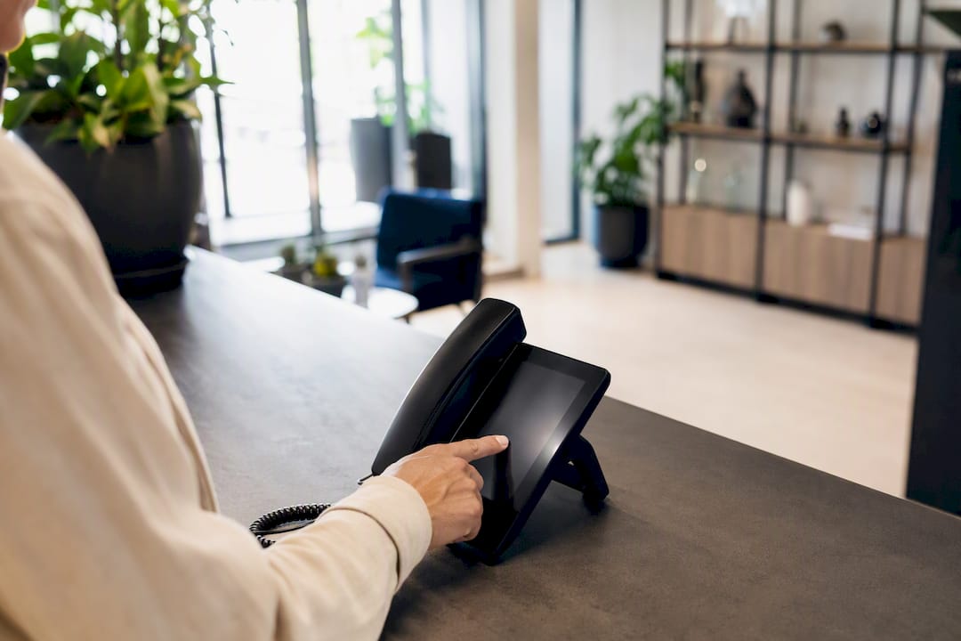 Eine Hand tippt auf das Tastenfeld eines Telefons im Büro einer Ferienwohnung.
