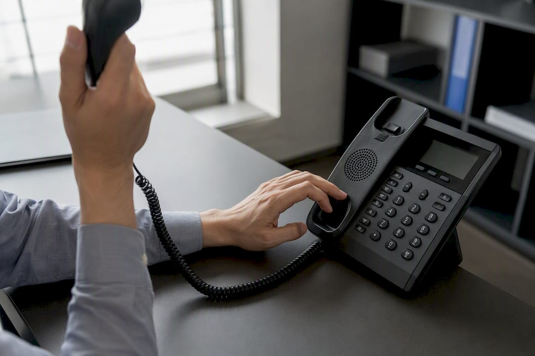 Hände beim Wählen einer Nummer am Bürotelefon