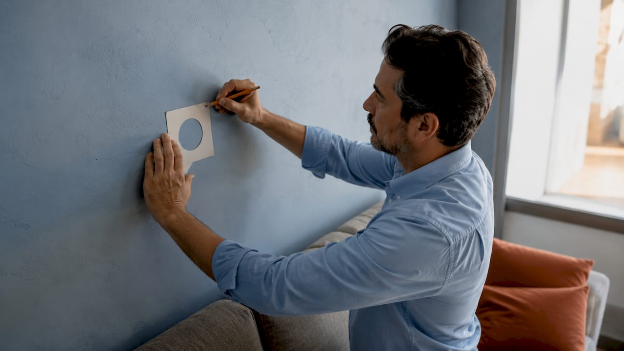 Hands marking gallery wall height on living room wall