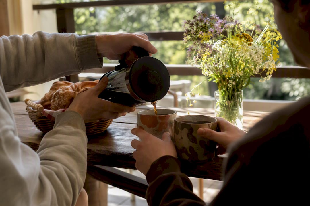 Hands pouring coffee into mugs at kitchen counter