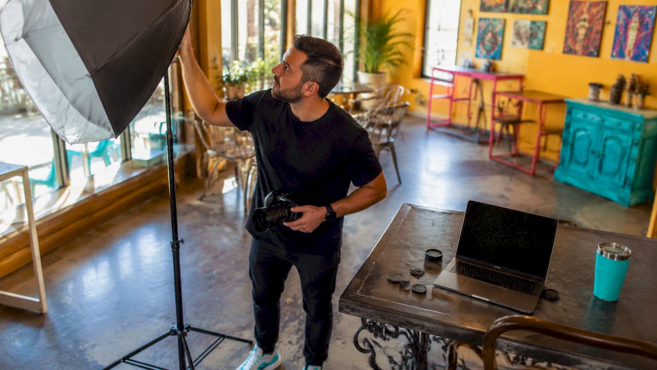 Person adjusting a studio light beside a laptop in a bright creative workspace