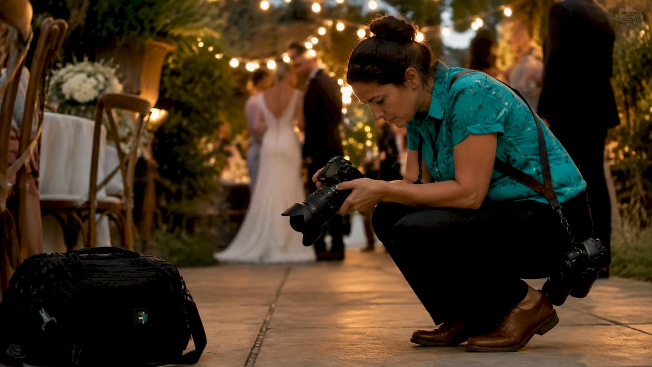 Photographer crouching to take a shot at an outdoor evening wedding reception with string lights