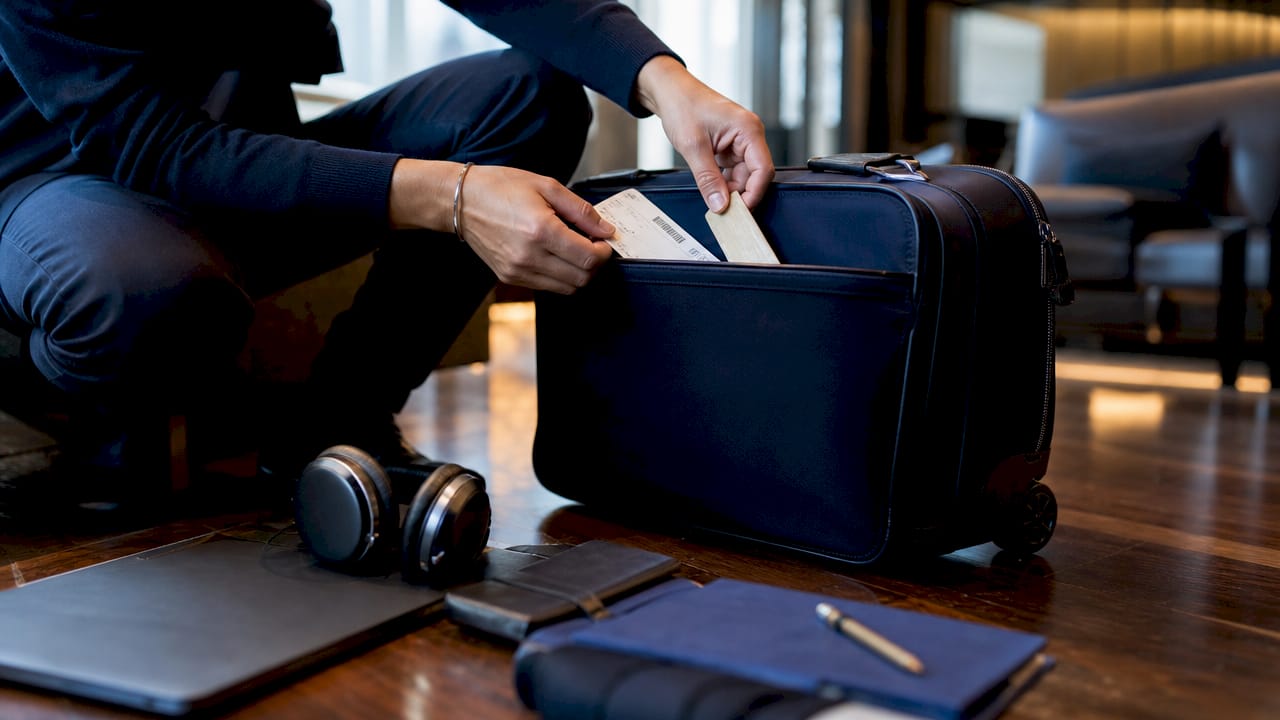 Hands packing boarding pass and baggage tag into suitcase