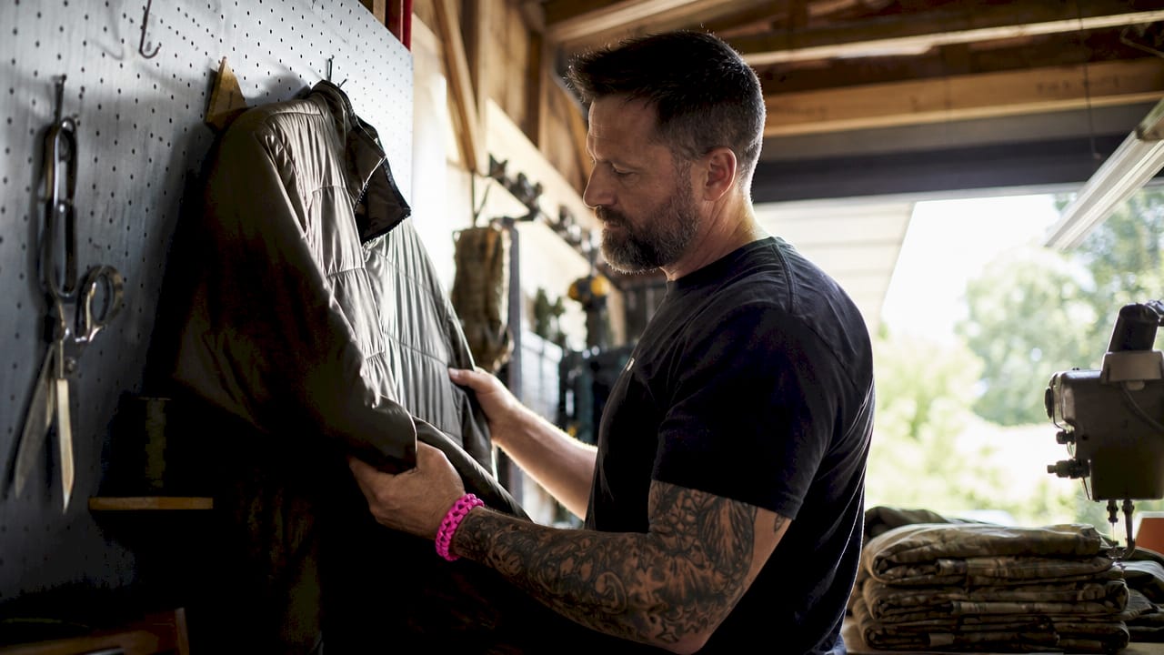Veteran inspecting insulated midlayer jacket indoors