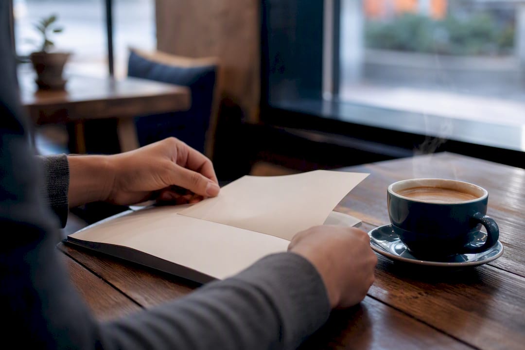 Hands flipping notebook page beside coffee cup