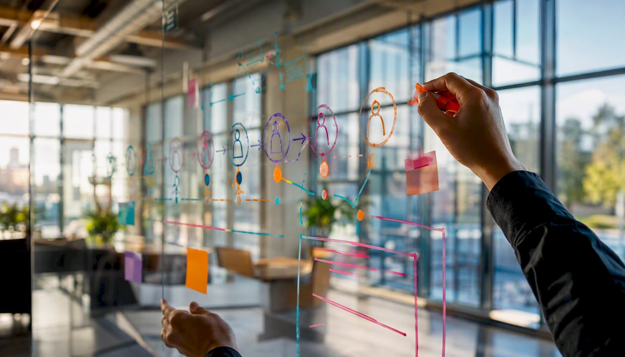 Hands mapping customer churn workflow on glass board