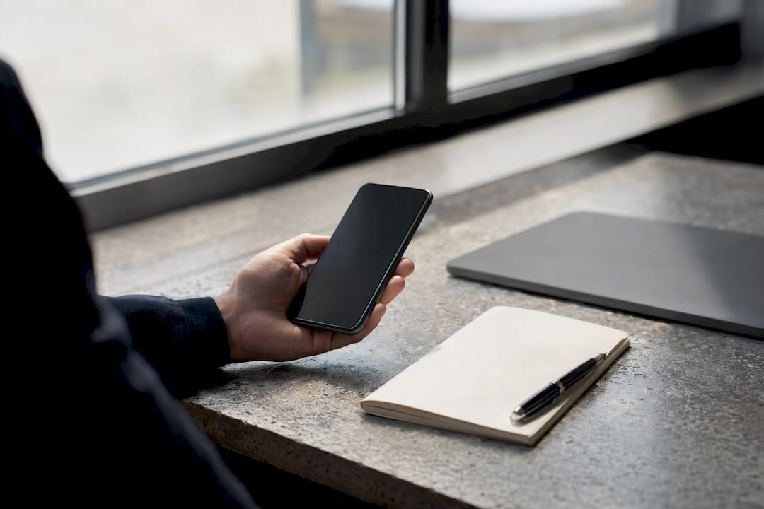 Hand holding phone with dark screen on desk