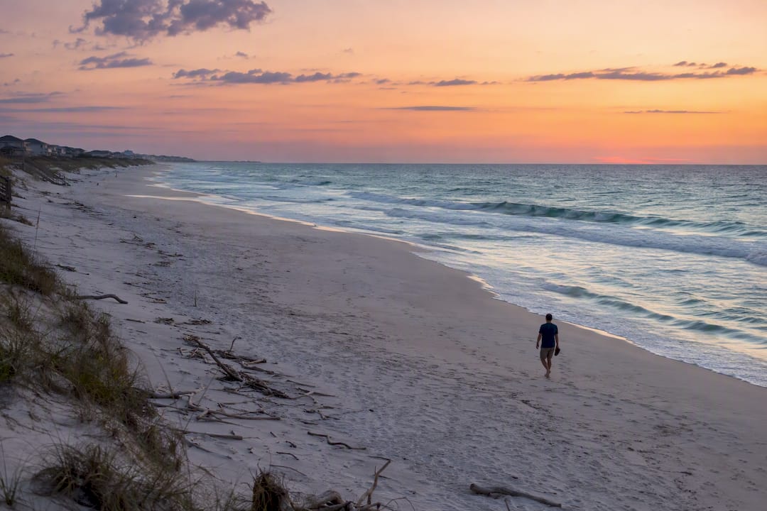 Traveler walking along long Inlet Beach shoreline at sunset