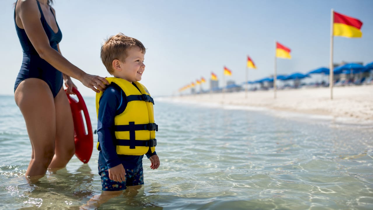 Child in life jacket near lifeguarded water
