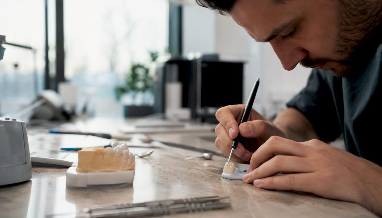Close-up of hands shaping a porcelain veneer in dental lab
