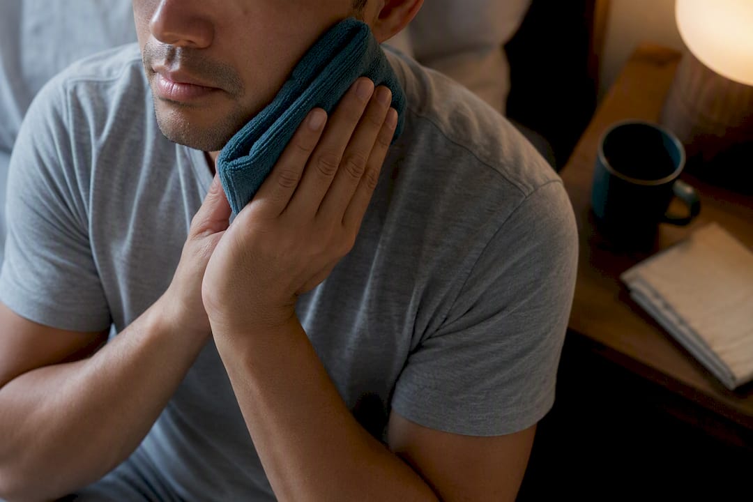Adult applying warm compress to jaw