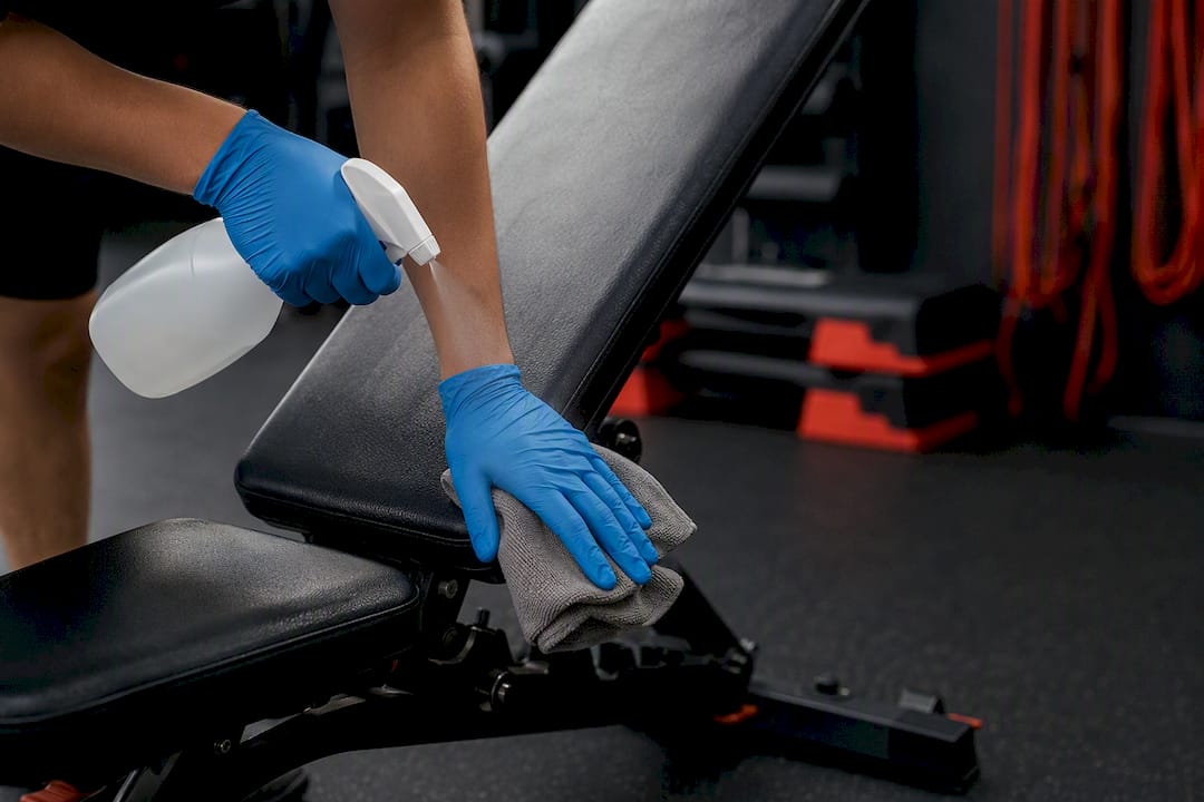 Gloved hands disinfecting gym barbell