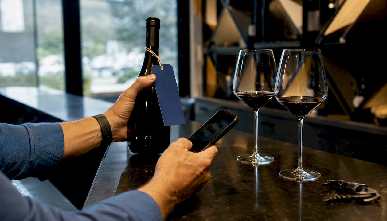 Hands comparing wine bottle and digital procurement data