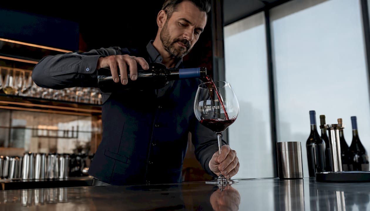 Sommelier pouring red wine into large glass at table