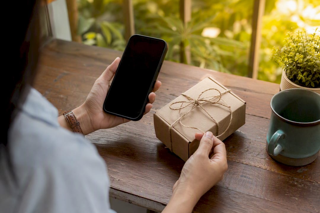 Hands tying sustainable gift with smartphone nearby