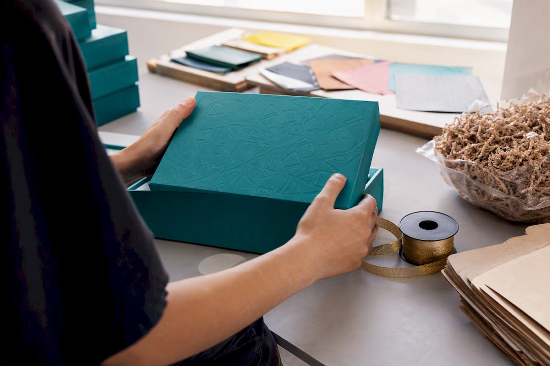 Hands folding teal gift box with ribbon and inserts