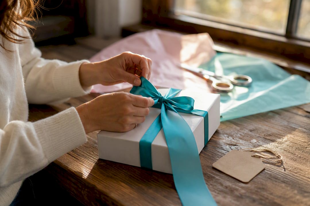 Hands tying teal ribbon on corporate gift box