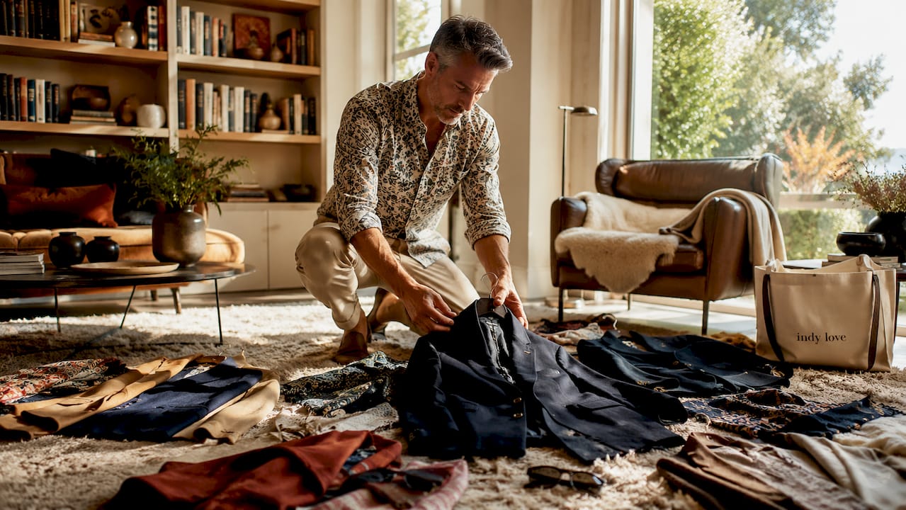 Man arranging classic and trendy wardrobe pieces at home