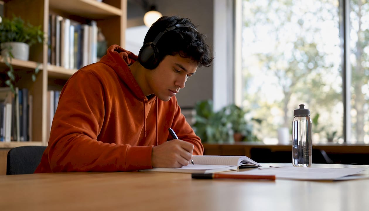 Alumno atento escuchando una clase de idiomas mientras apunta lo más importante en su cuaderno.