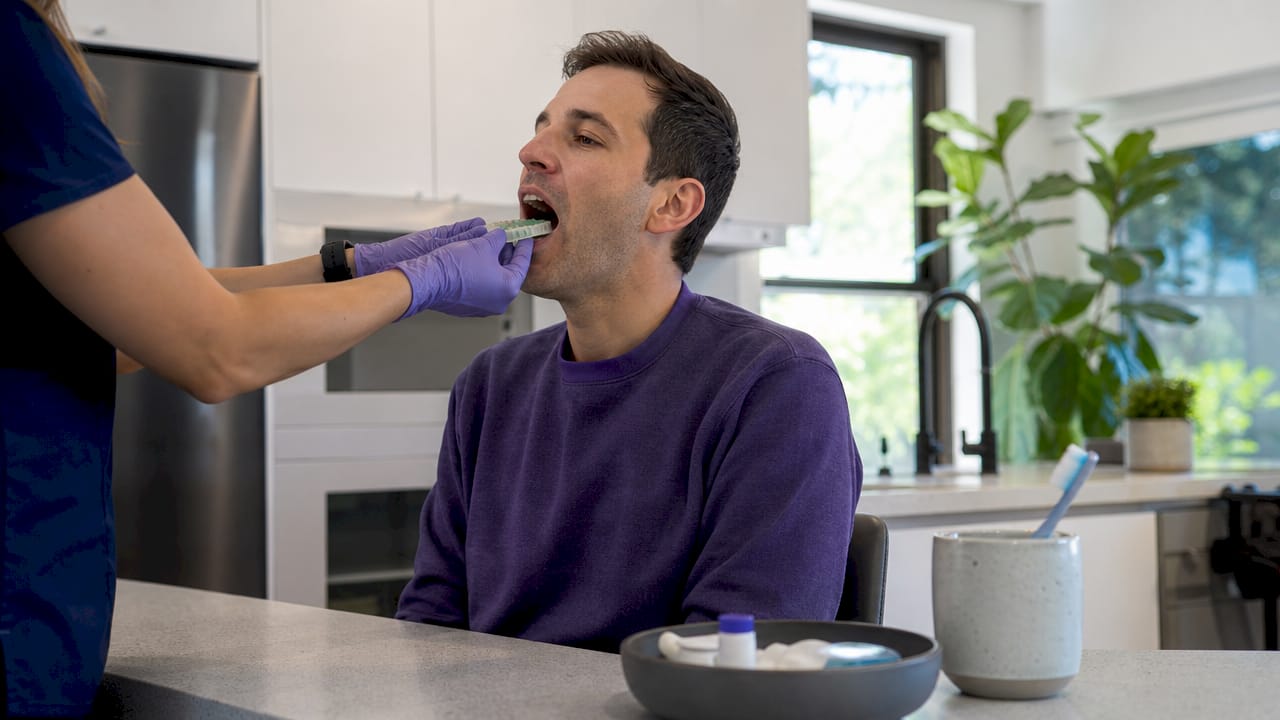 Hands placing dental impression tray in mouth at home
