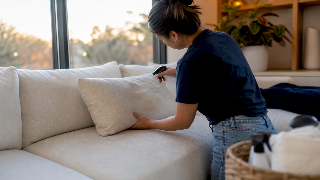 Hands spraying cleaner on couch upholstery