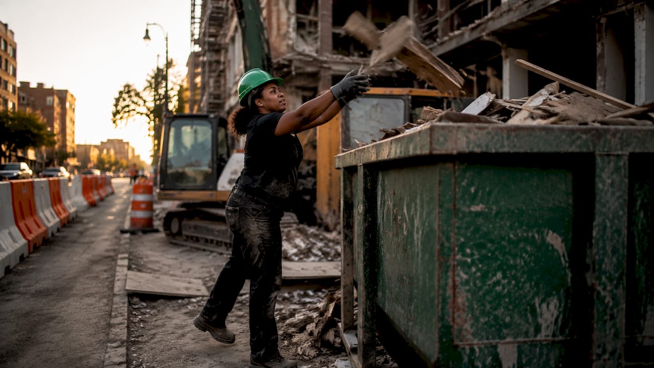 Worker loading debris into roll-off dumpster
