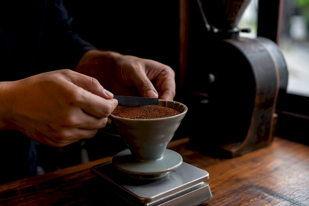 Hands leveling coffee grounds in moka basket on scale
