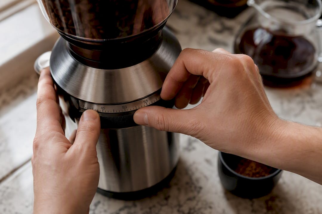 Hands adjusting coffee grinder for medium-fine grounds