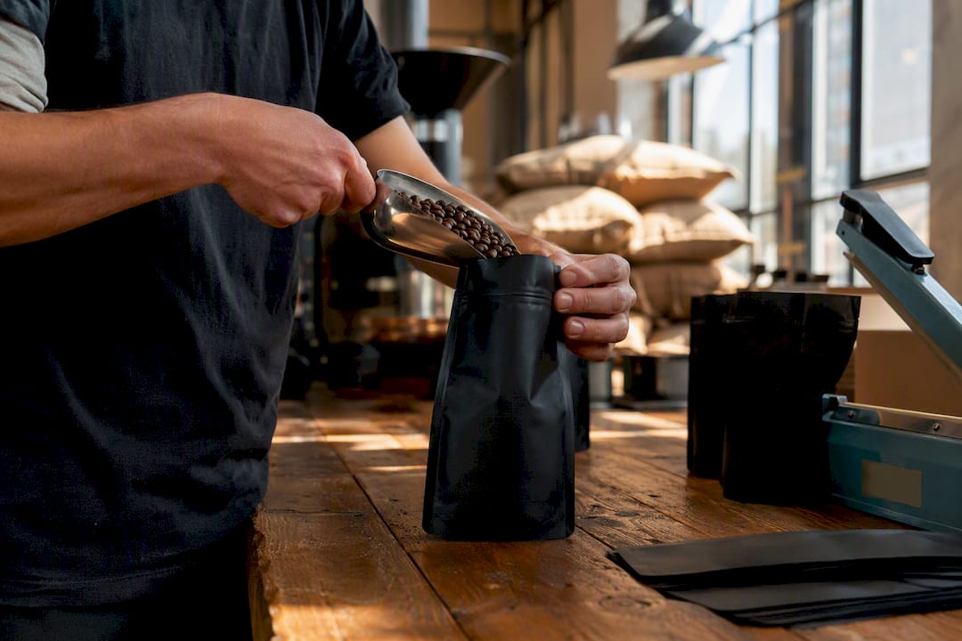 Hands filling fresh coffee bags in roastery