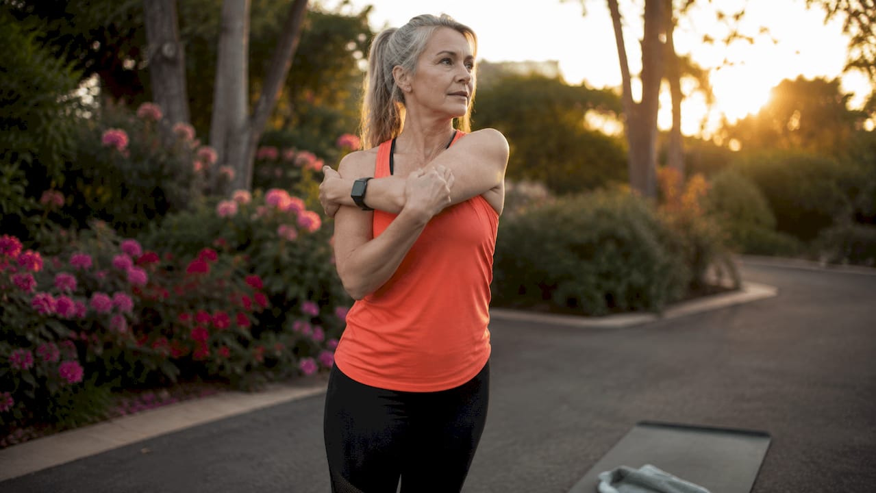 Mature woman tying running shoes outdoors