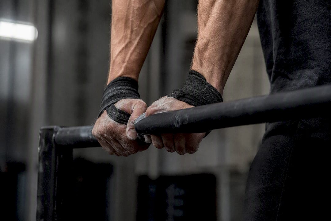 Hands gripping parallel bars with wrist straps