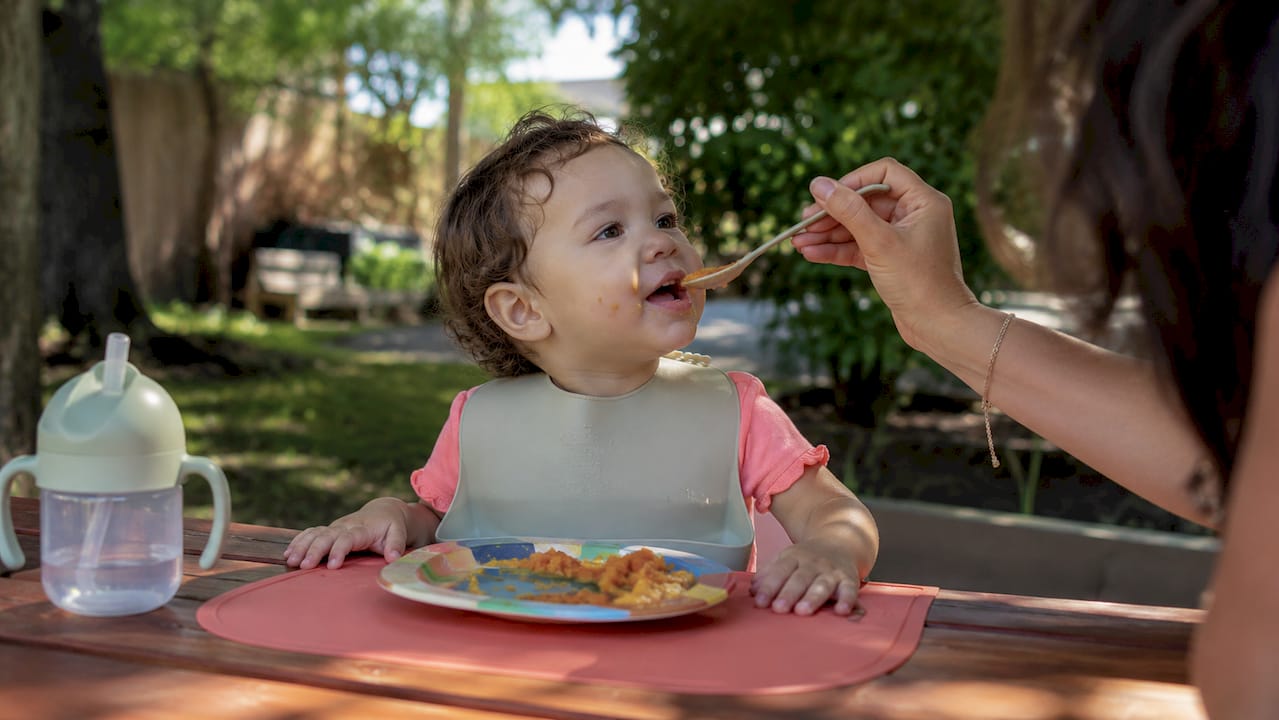 Toddler eating mashed sweet potatoes at table
