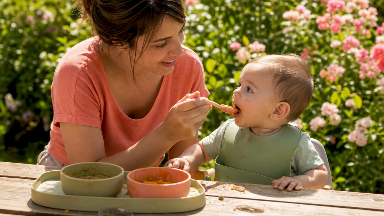 Hands feeding baby iron-rich pureed food at table