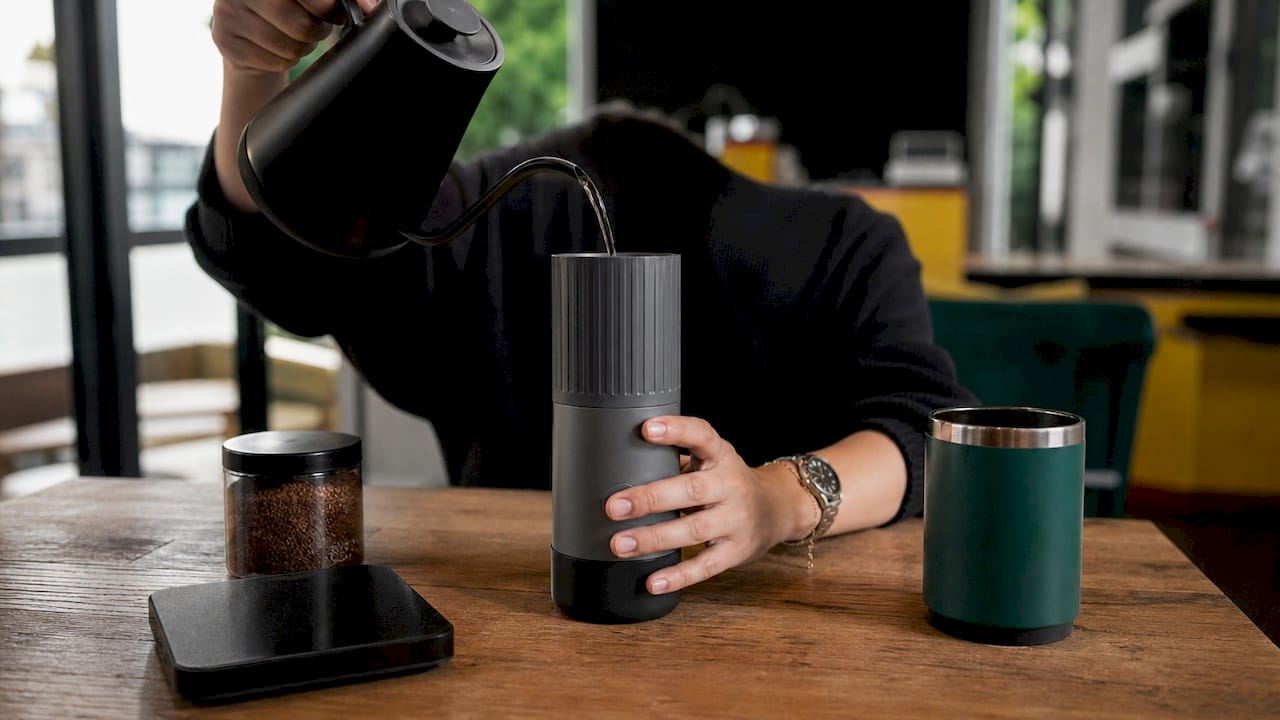 Hands using portable coffee brewer at home office desk