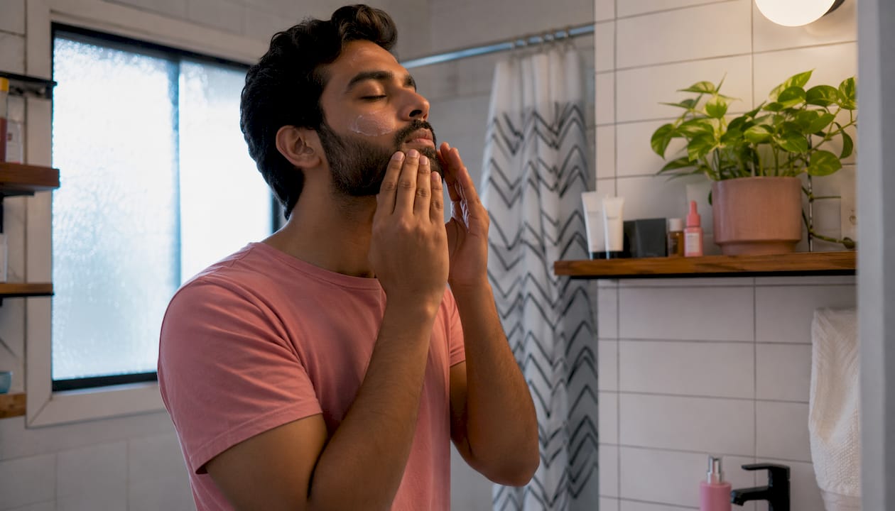 Man applying lightweight moisturizer in bedroom