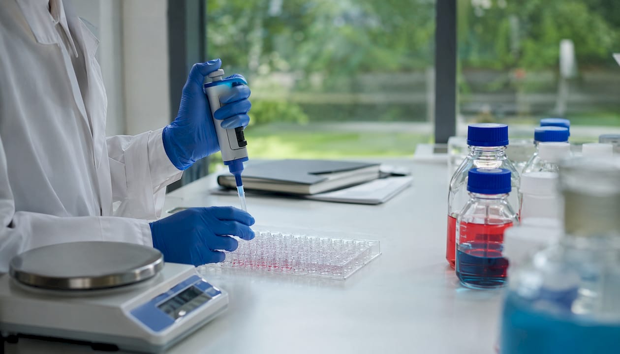 Gloved hands pipetting on a lab bench