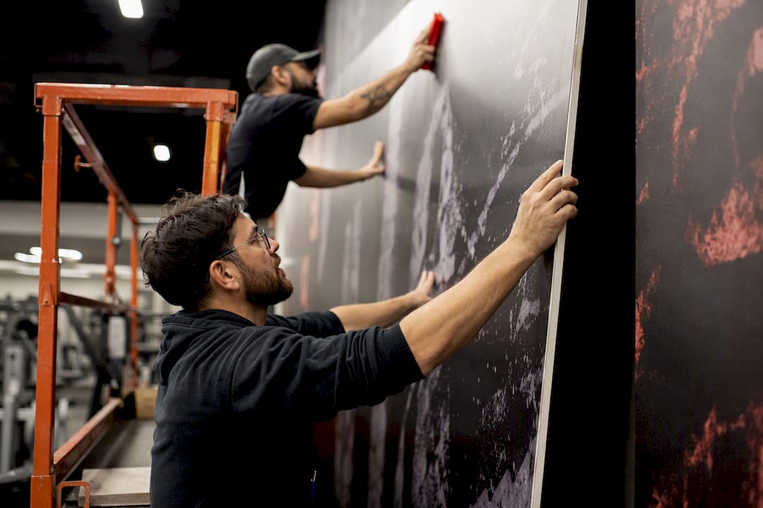 Installers hanging gym wall mural on scaffolding