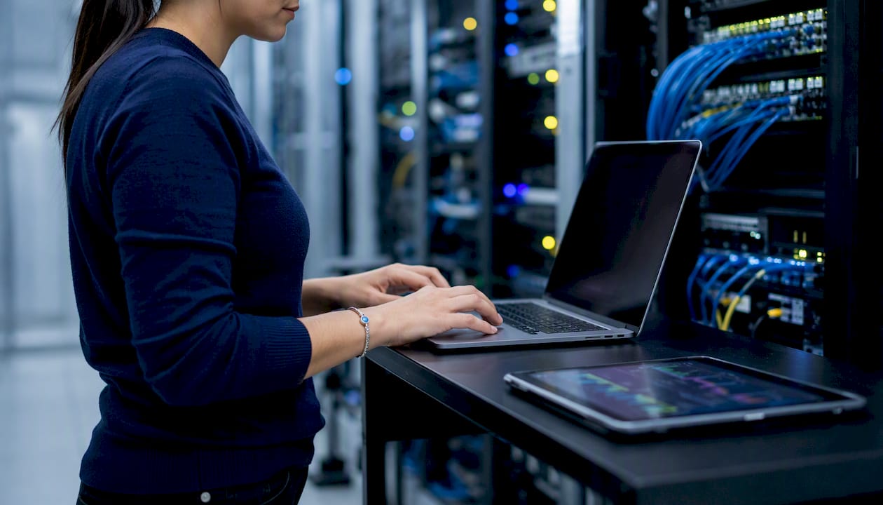 Hands typing on laptop in server rack aisle