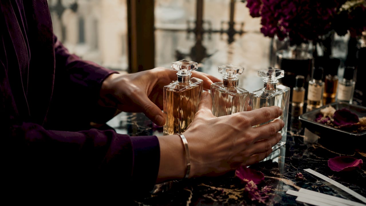 Zoom sur des mains qui tiennent délicatement des flacons de parfum.