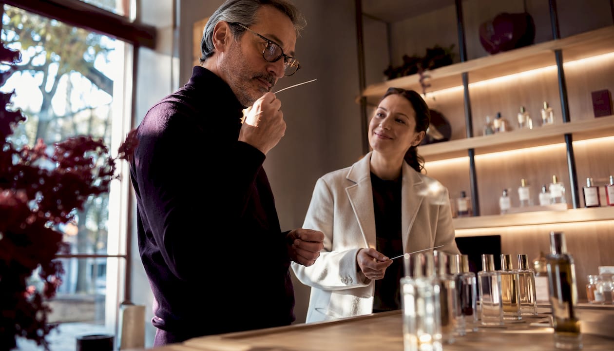 Una clienta conversa con la dependienta sobre diferentes perfumes en la tienda, buscando recomendaciones y comparando fragancias antes de decidir cuál llevarse.