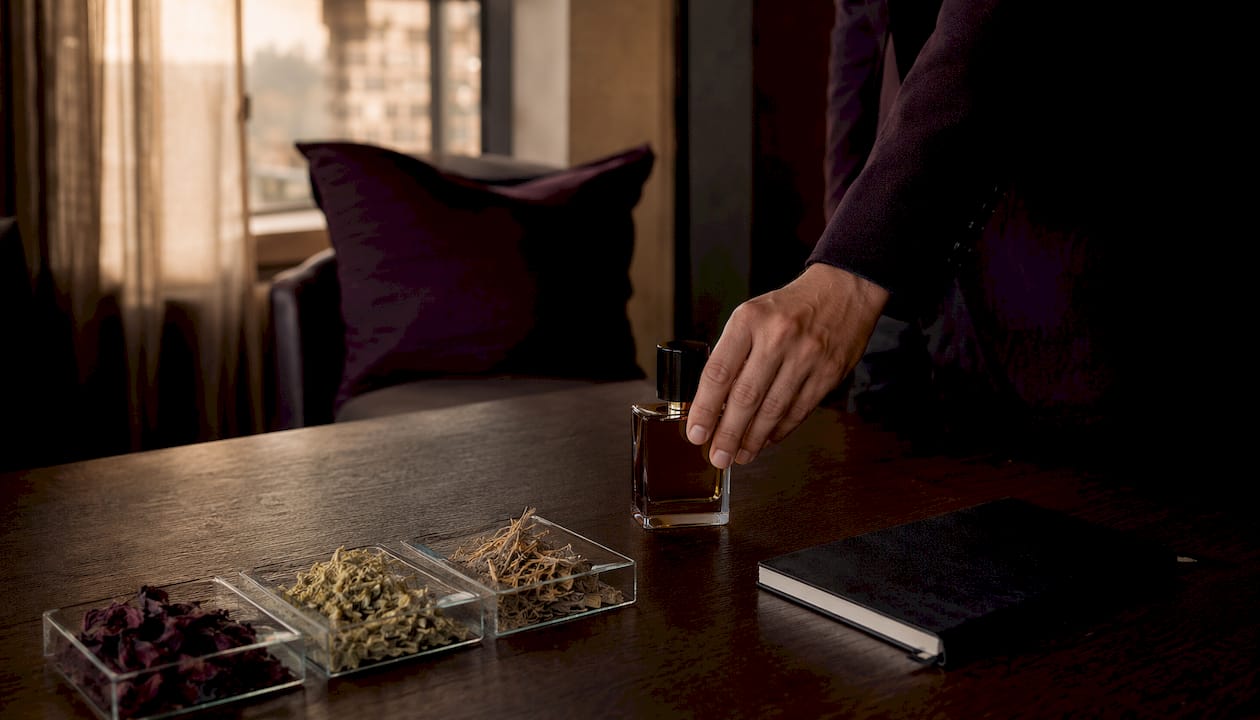 Une main dépose délicatement un flacon de parfum sur une table en marbre.