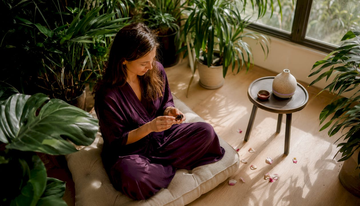 Des mains enveloppent délicatement un flacon d’huile essentielle de bois de santal pendant une séance de méditation.